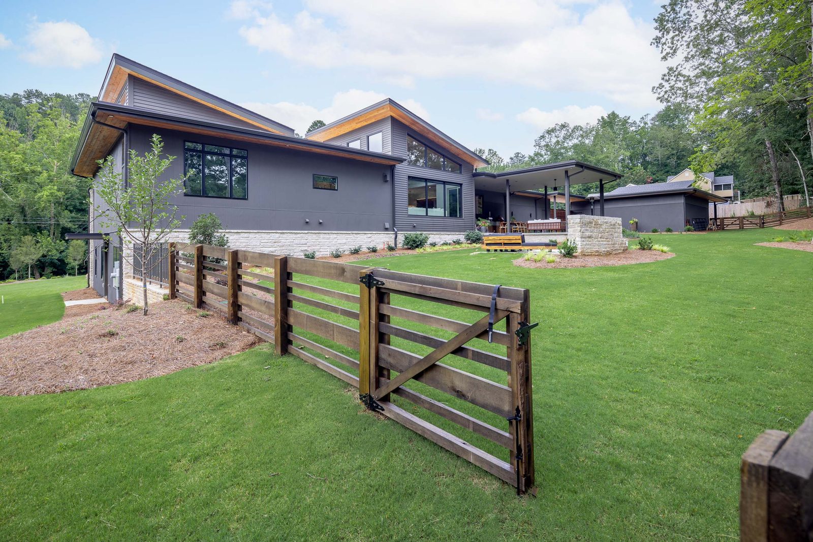 View up the lawn to the house past the wood farm gate — The Ortiz Home, custom home built by Ironwood Construction Group in Sugar Hill, Georgia