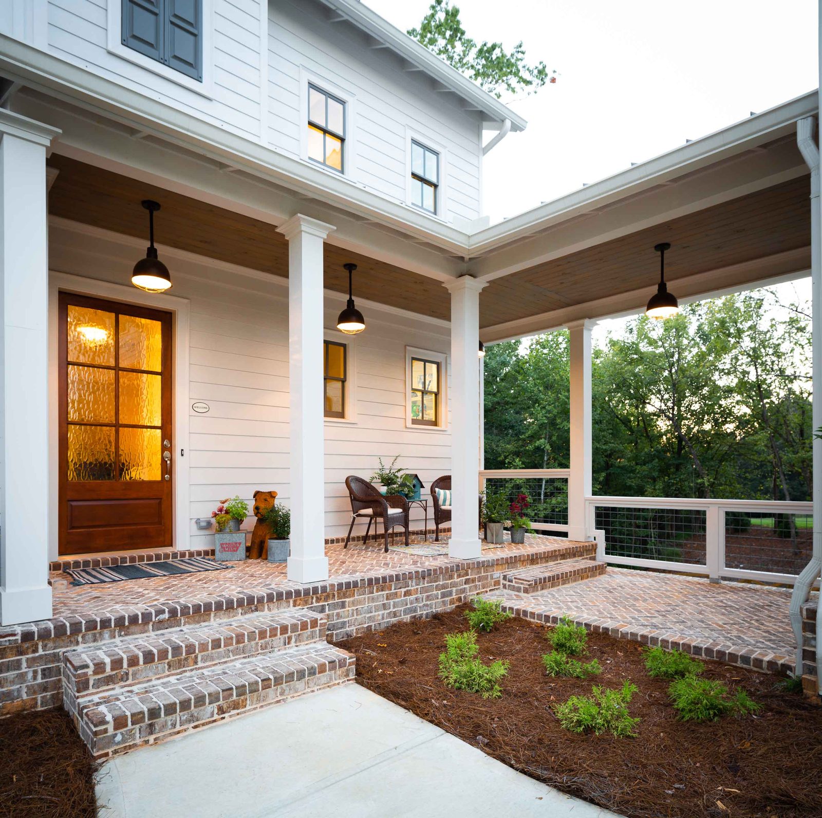 Front porch with brick steps and wood front door at dusk — Austin Garner Rd, custom home built by Ironwood Construction Group