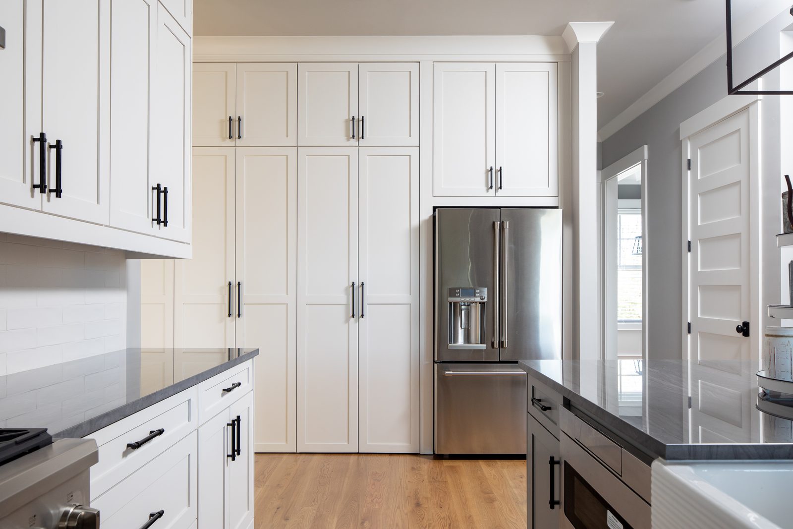 Kitchen cabinetry with counter-depth refrigerator and dark counters — Spring 2020 Custom Home, custom home built by Ironwood Construction Group